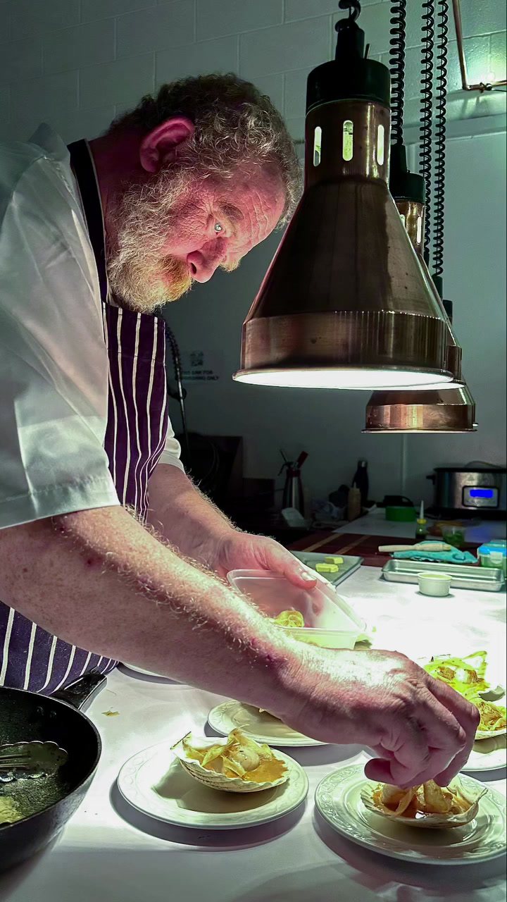 Adrian plating scallops in their shells under a copper lamp