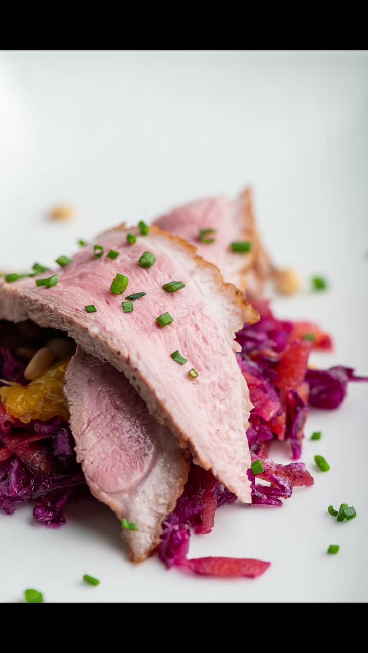 Sliced duck breast served over red cabbage with a scattering of chives