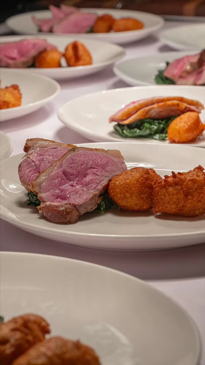 A row of plated Sunday lunches with lamb, crispy potatoes and greens ready to serve