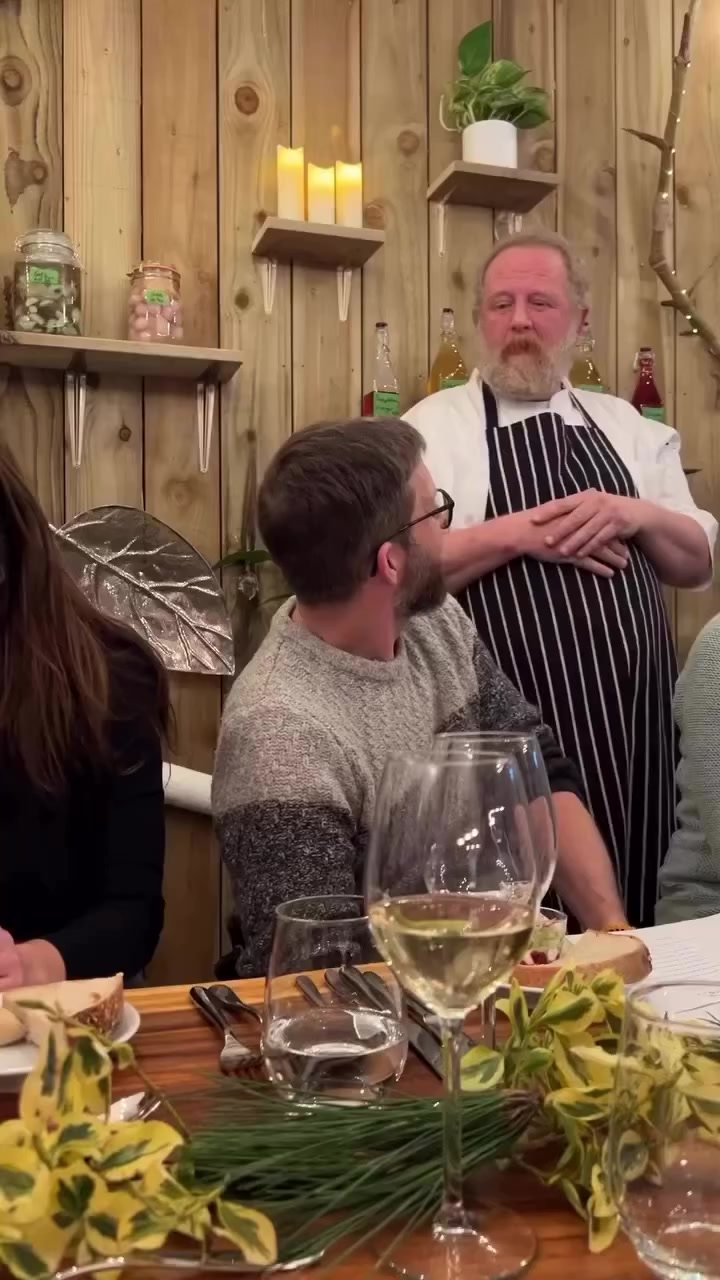 Adrian talking with a guest seated at the Chef's Table, wine glasses on the table