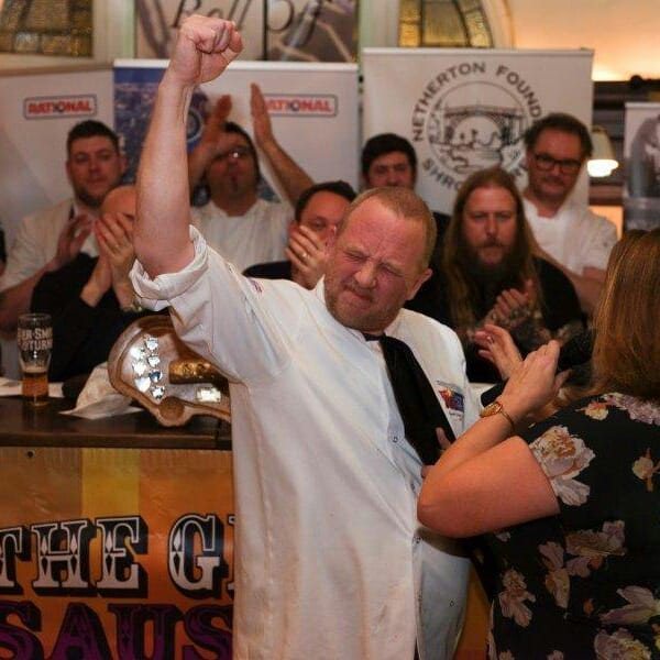 Adrian Oliver raising a trophy, surrounded by fellow chefs applauding